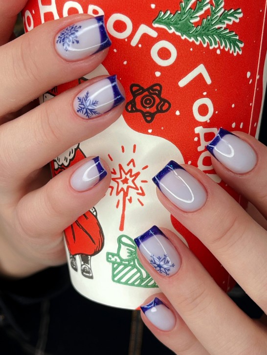 Зимний френч с синими снежинками в Архангельске, салон красоты "Мускат". Новогодний дизайн ногтей на форме "мягкий квадрат": синий гель-лак и акцентный рисунок. На фото рука держит красный стакан с новогодним принтом.